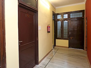 Un pasillo con un extintor de incendios fijado en la pared, una puerta con la leyenda 'F-3', y un par de puertas dobles con paneles de vidrio.