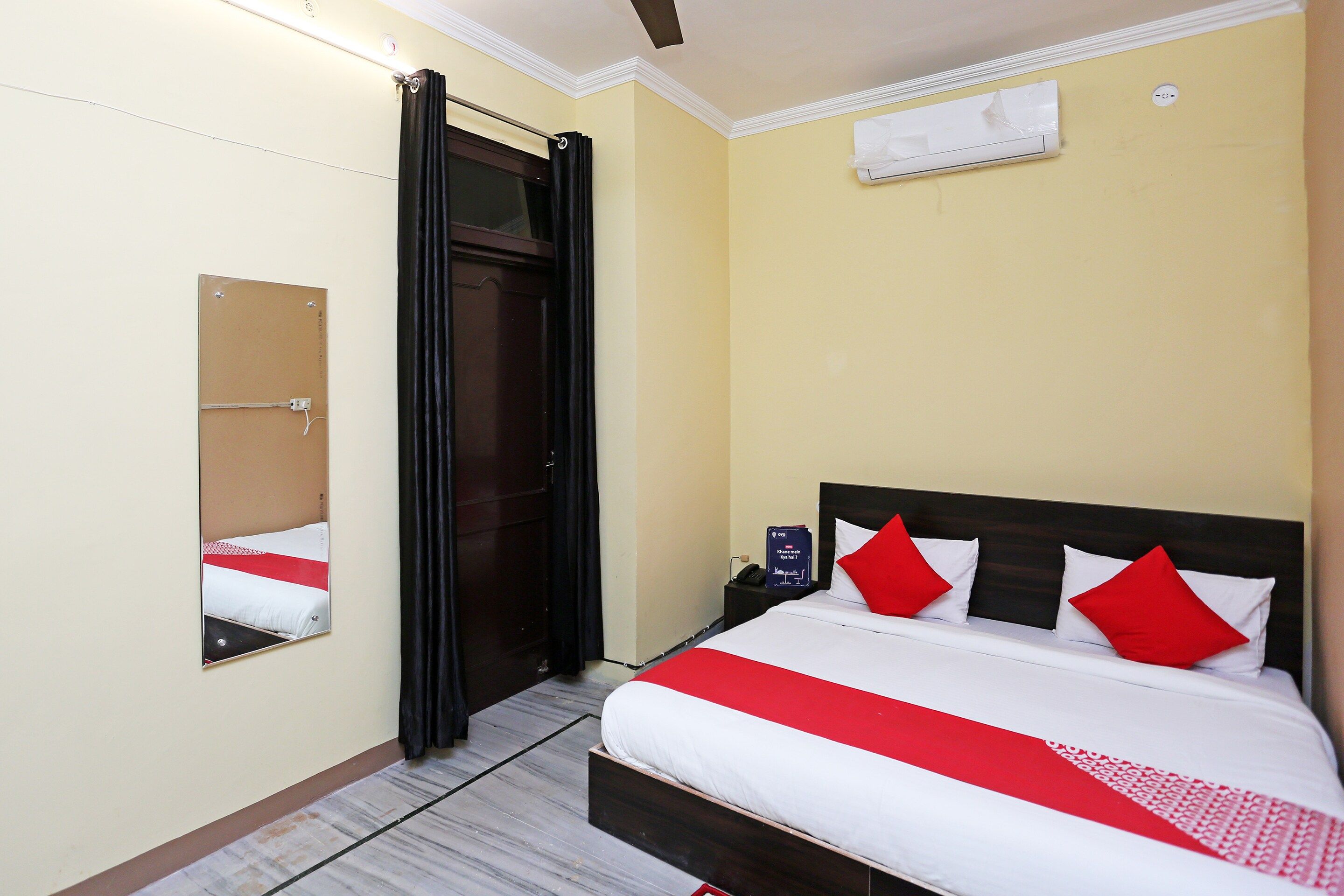 A hotel room with a bed, a bedside table, a mirror, and a door.
