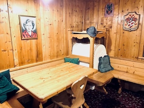 A wooden interior with a wooden table and benches, a framed picture on the wall, and a coat hanging on a hook. - garni col da la vila (Penia di Canazei)