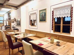 A restaurant with wooden tables and chairs, a counter with food items, and framed artwork on the walls. - garni col da la vila (Canazei)