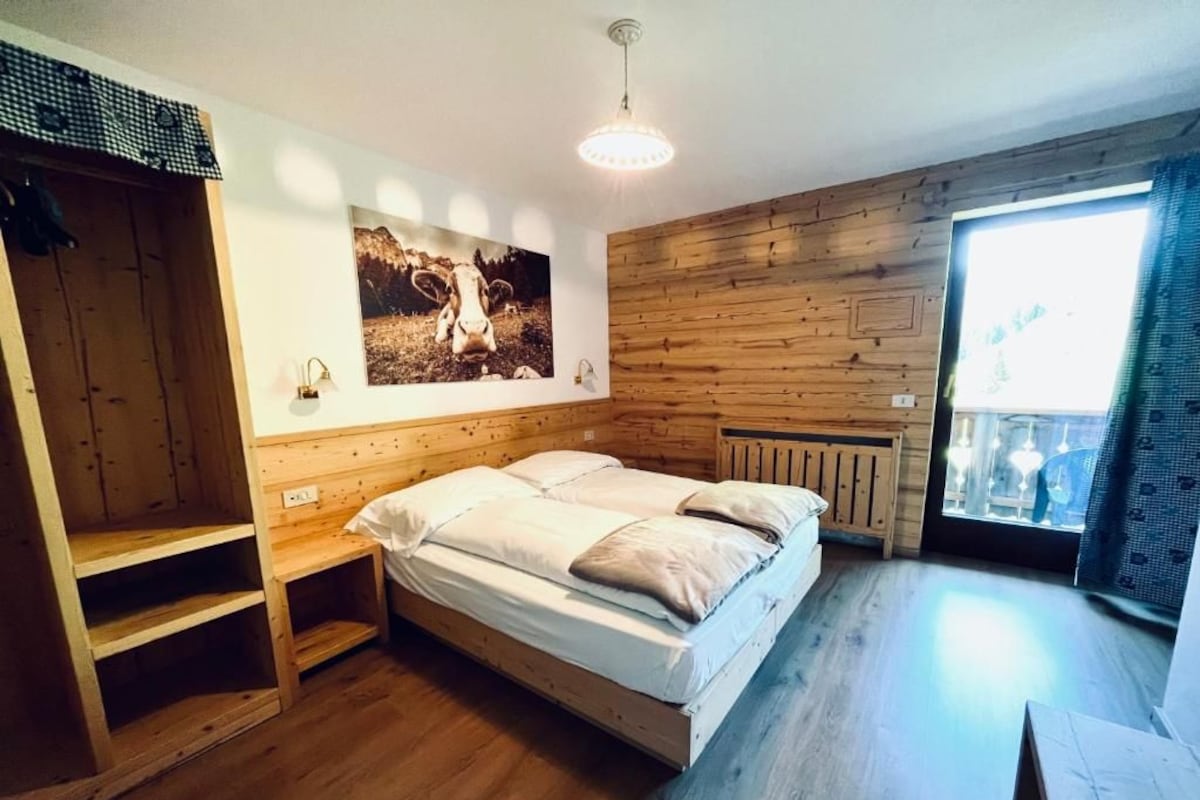 Un dormitorio con cama de madera, un radiador fijado a la pared, una ventana con cortinas y una estantería.