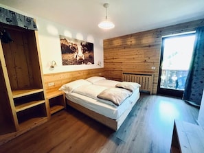 Un dormitorio con cama de madera, un radiador fijado a la pared, una ventana con cortinas y una estantería.