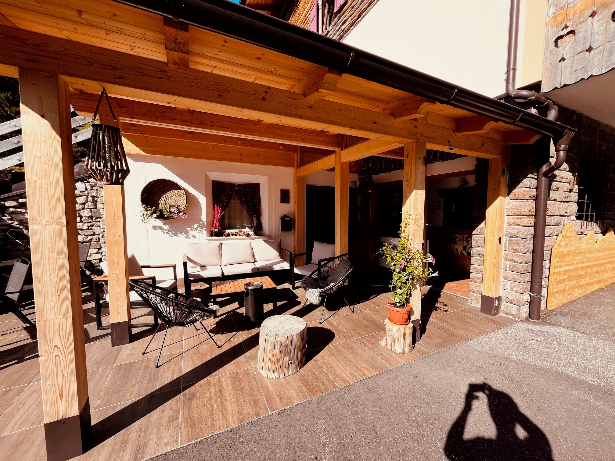 Un área de patio al aire libre con vigas de madera, un sofá, sillas, una mesa y una planta en maceta.