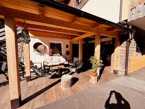 An outdoor patio area with wooden beams, a sofa, chairs, a table, and a potted plant. - garni col da la vila (Canazei)