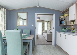 En kompakt opholdsstue med spiseplads, tekøkken og sofa i baggrunden.