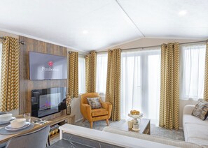 A modern living room with a flat-screen TV, a comfortable armchair, a sofa, and a dining area with a table set for two. - The Luxe with Hot Tub and enclosed garden (Hayle)