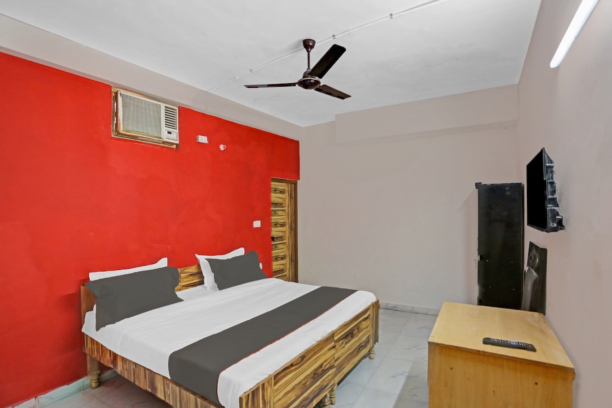 A bedroom with a bed, a ceiling fan, a small wooden desk, and a television.