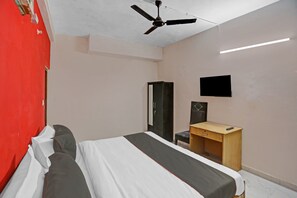 A bedroom with a bed, a desk, a wardrobe, a ceiling fan, and a flat-screen TV. - Hotel O Golden (Noida)