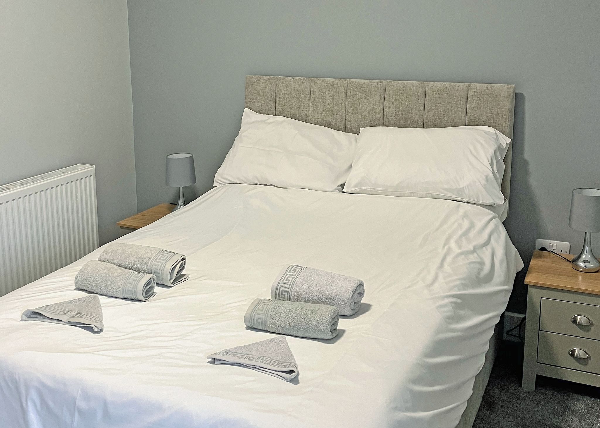 A neatly made bed with white linens, two pillows, and three folded towels.