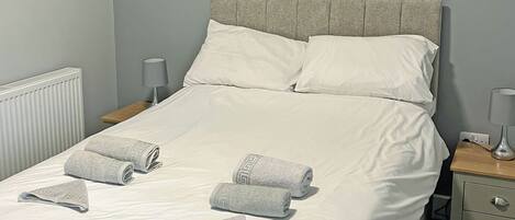 A neatly made bed with white linens, two pillows, and three folded towels.