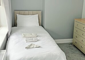 A neatly made bed with white linens and a headboard, a wooden dresser with drawers, and a window with curtains. - A beautifully restored two-storey, two bedroom cottage sleeping four people. (Filey)