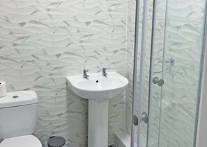 Ein Badezimmer mit weißer Marmorwand, einem Standwaschbecken, einer Toilette und einer Duschkabine aus Glas.