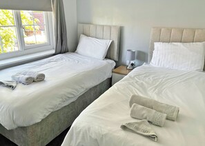 A hotel room with two beds, each with white linens and pillows, a bedside table with a lamp, and a window with curtains. - A beautifully restored two-storey, two bedroom cottage sleeping four people. (Filey)