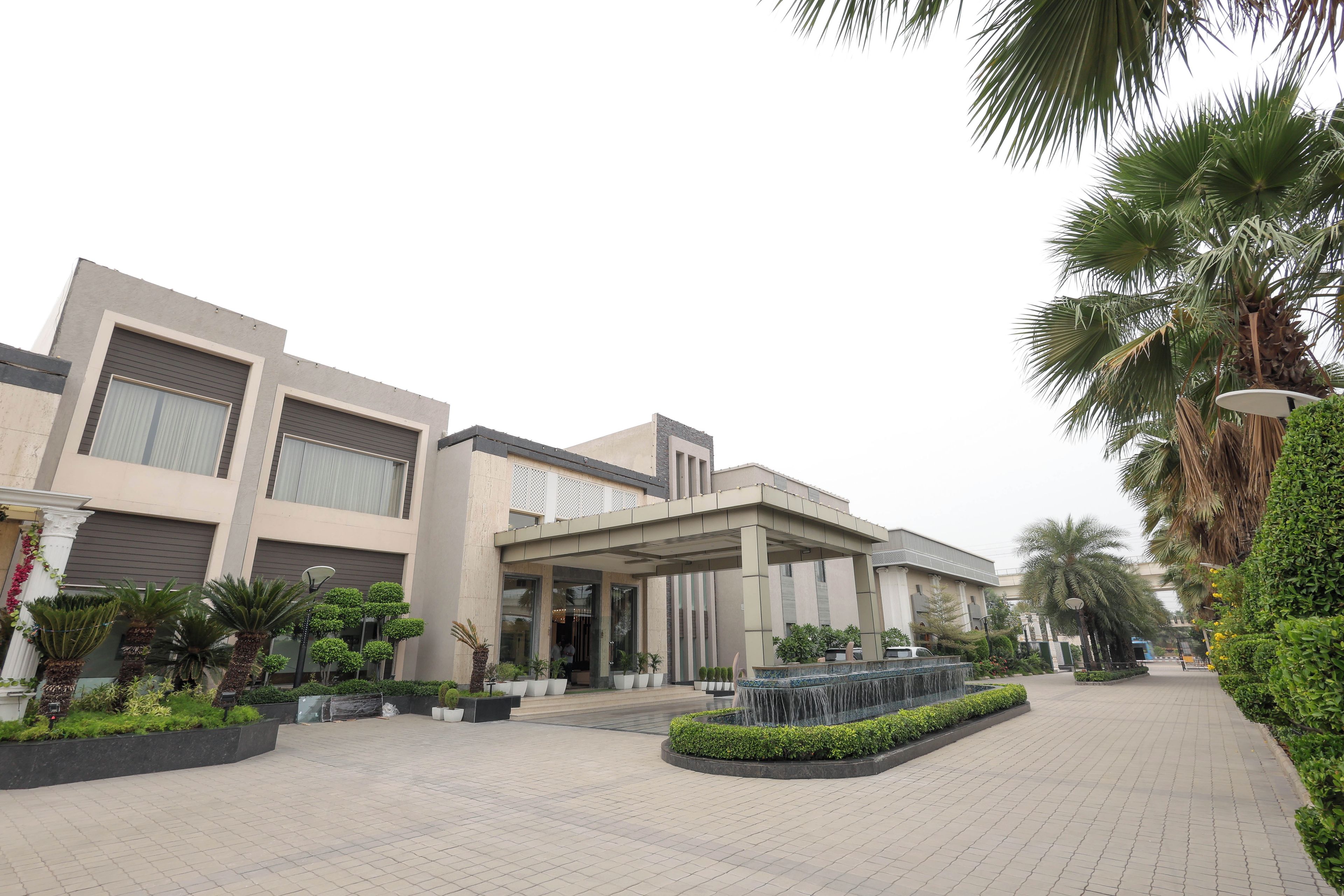 A modern building with a covered entrance, paved walkway, and landscaped areas with palm trees and shrubs.
