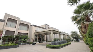 A modern building with a covered entrance, paved walkway, and landscaped areas with palm trees and shrubs.