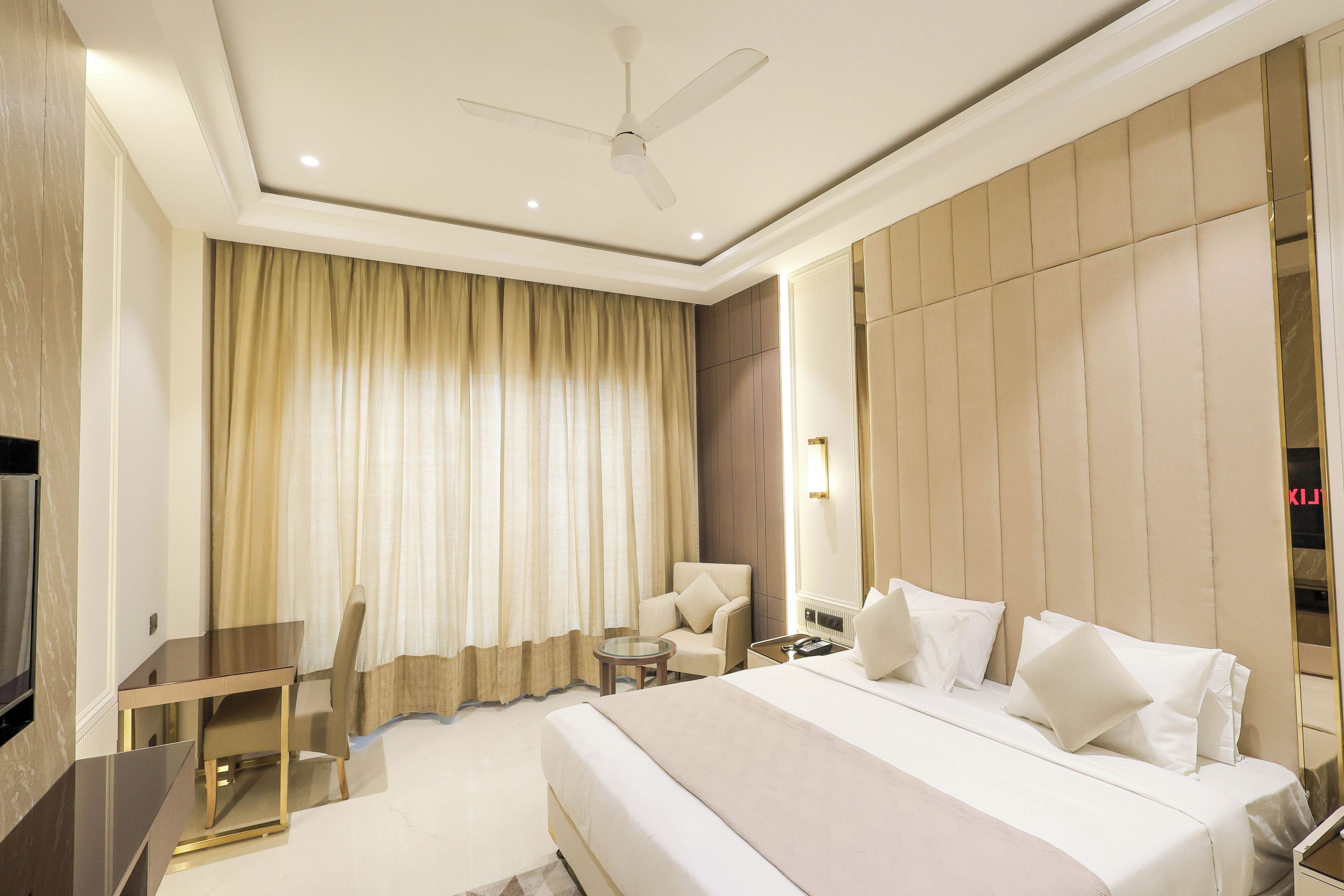 A hotel room with a large bed, a chair, a small table, and a ceiling fan.