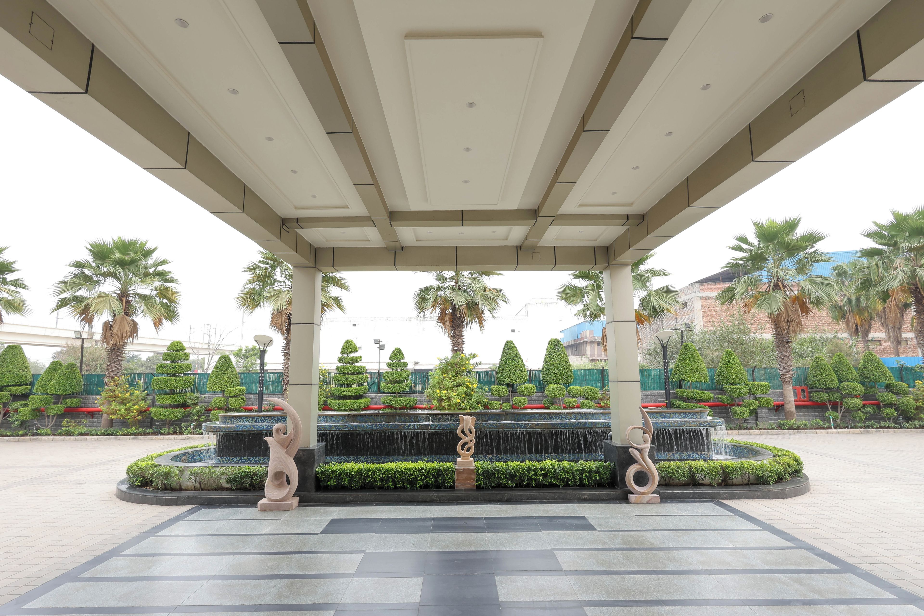 A covered outdoor area with a fountain, palm trees, and neatly trimmed bushes.