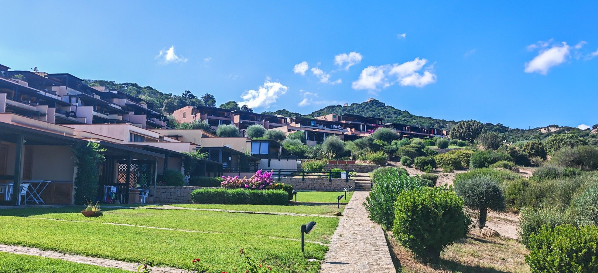A hillside residential area with modern houses, a paved pathway, and a grassy lawn.