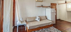 A compact room with a bed, a small table with a lamp, a refrigerator, and a window with curtains. - Casa Tanca Manna - View of Caprera & La Maddalena (Tanca Manna)