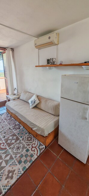 A compact room with a sofa bed, a refrigerator, a wall-mounted air conditioner, and a patterned rug. - Casa Tanca Manna - View of Caprera & La Maddalena (Tanca Manna)