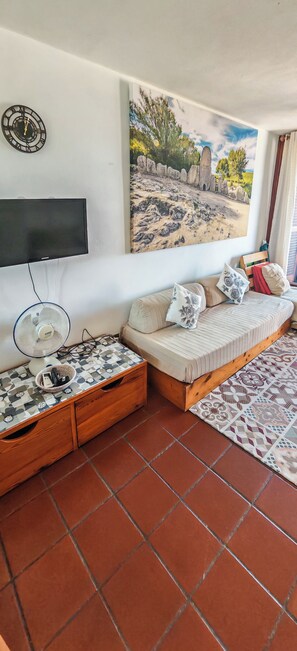 Ein Wohnzimmer mit einer Couch, einem Flachbildfernseher, einer Wanduhr und einem Gemälde.