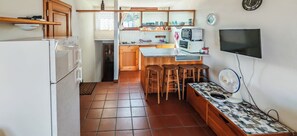A compact kitchen with a refrigerator, a microwave, a toaster, and a television. There are wooden stools and a patterned table. - Casa Tanca Manna (Tanca Manna)