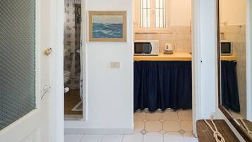Ein Flur, der zu einem Badezimmer mit Dusche, Mikrowelle und Toilette führt.