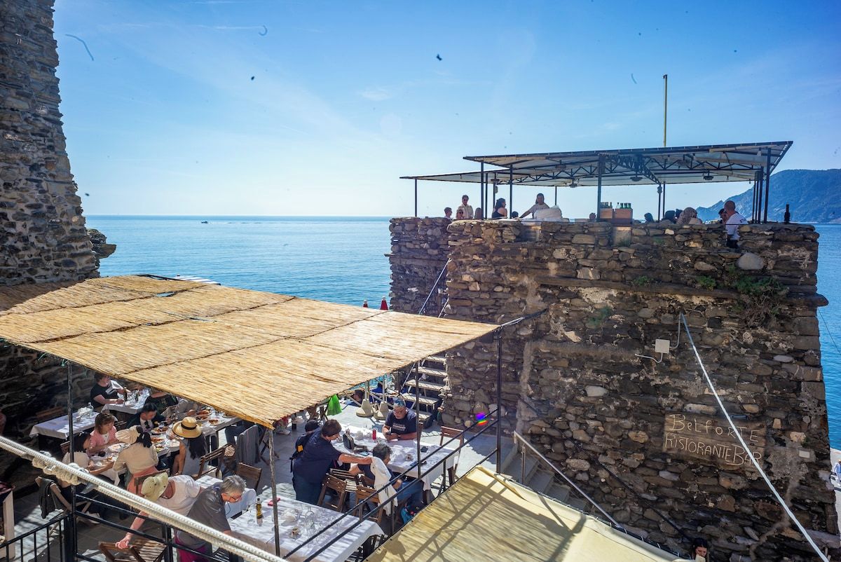 Un restaurante frente al mar con terraza al aire libre, paredes de piedra y vistas despejadas del océano.