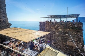 Un restaurant a la vora del mar amb terrassa a l'aire lliure i vistes a l'oceà, parets de pedra i una vista clara del mar.