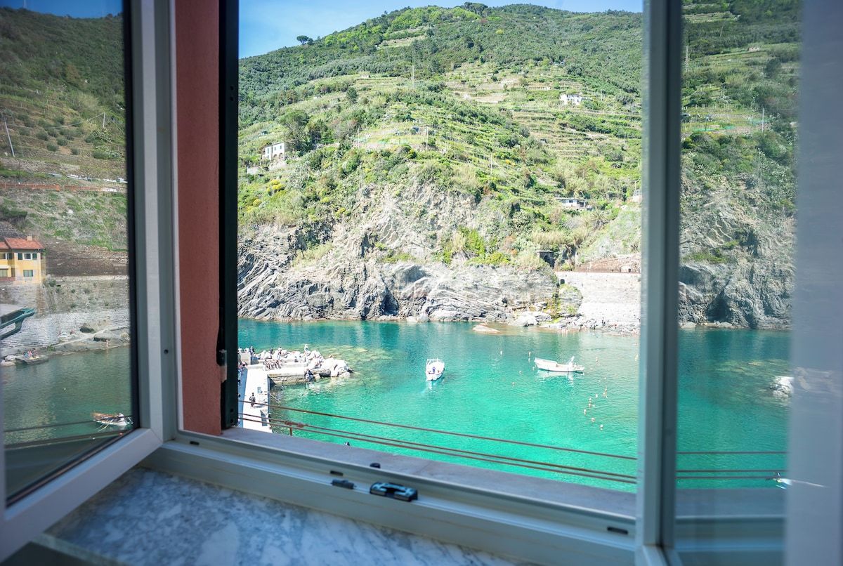 Vista costera desde una ventana con una imagen despejada de un mar turquesa, acantilados rocosos y algunas embarcaciones.
