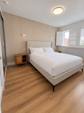 Un dormitorio con cama, mesita de noche, radiador y ventana con persianas.