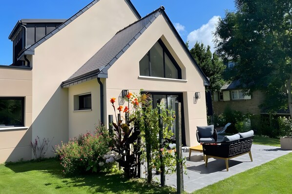 A modern house with a sloped roof, a large window, and a well-maintained garden with various plants and flowers.