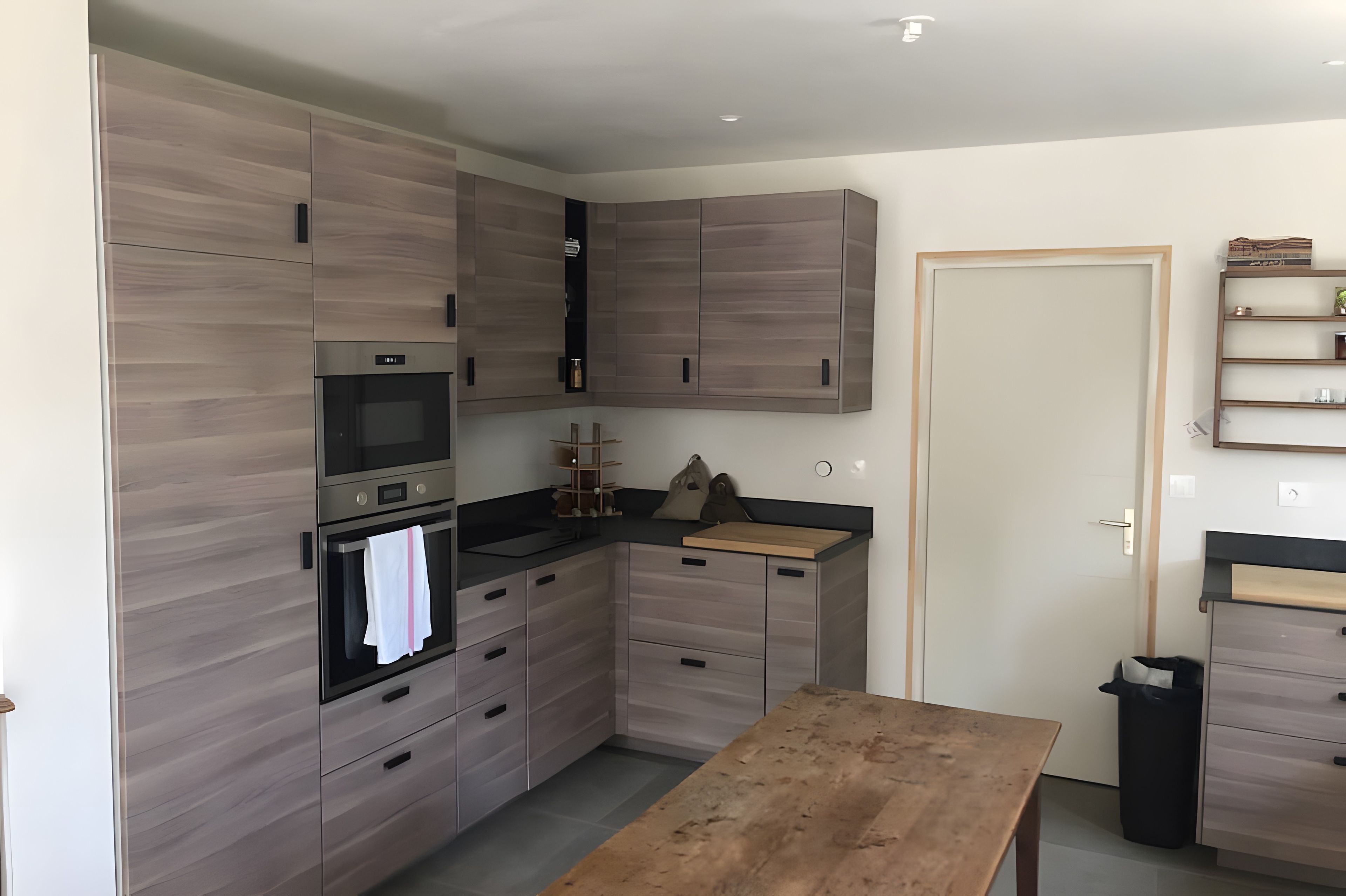 Een moderne keuken met inbouwapparatuur, een houten tafel en een prullenbak.