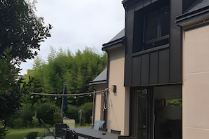 Moderni talo, jossa on patio, ulkovalot ja näkymä ympäröivään vihreään maisemaan.