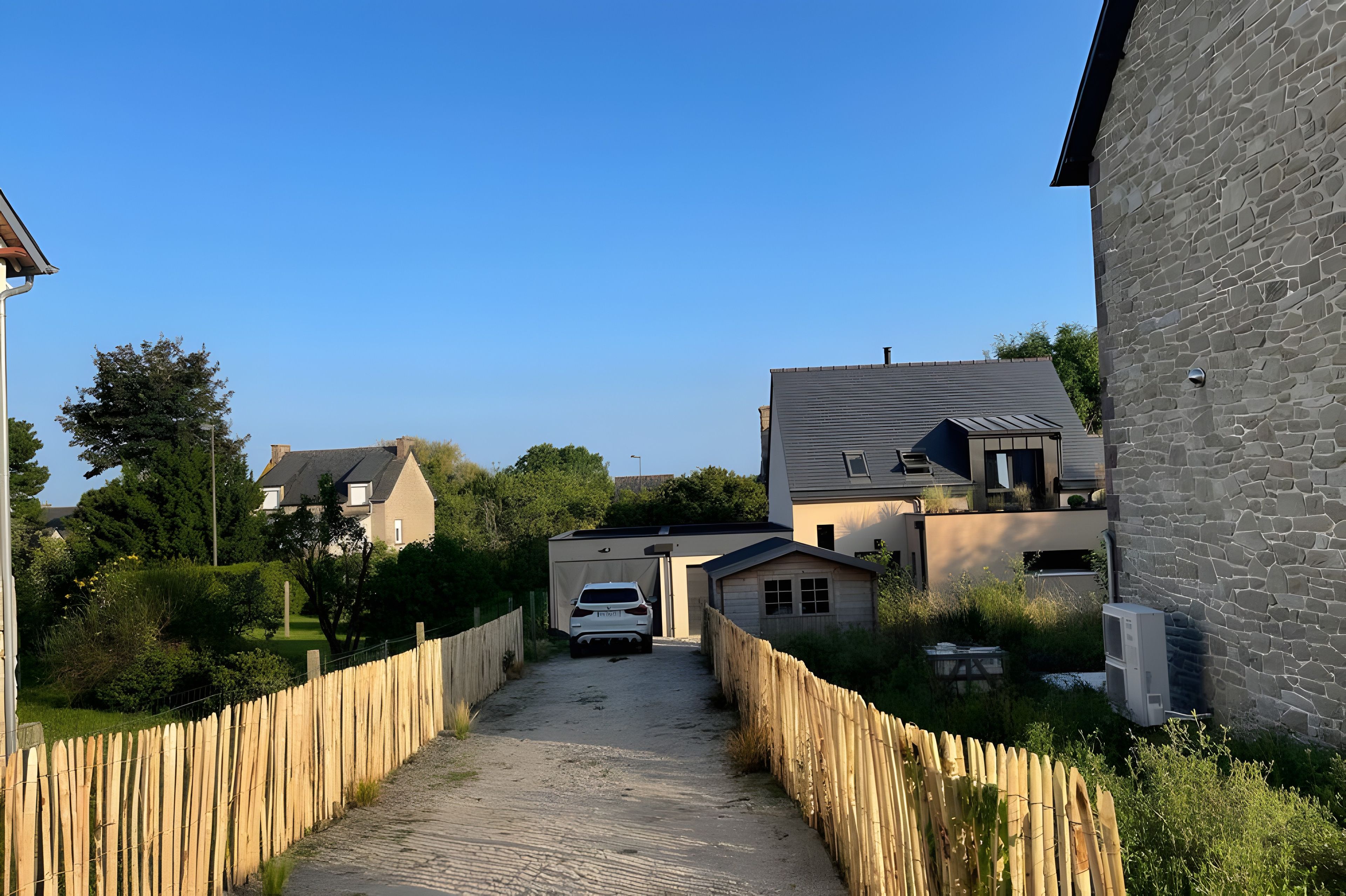 A residential street with houses, a white car parked in front of a garage, and a wooden fence along the road.