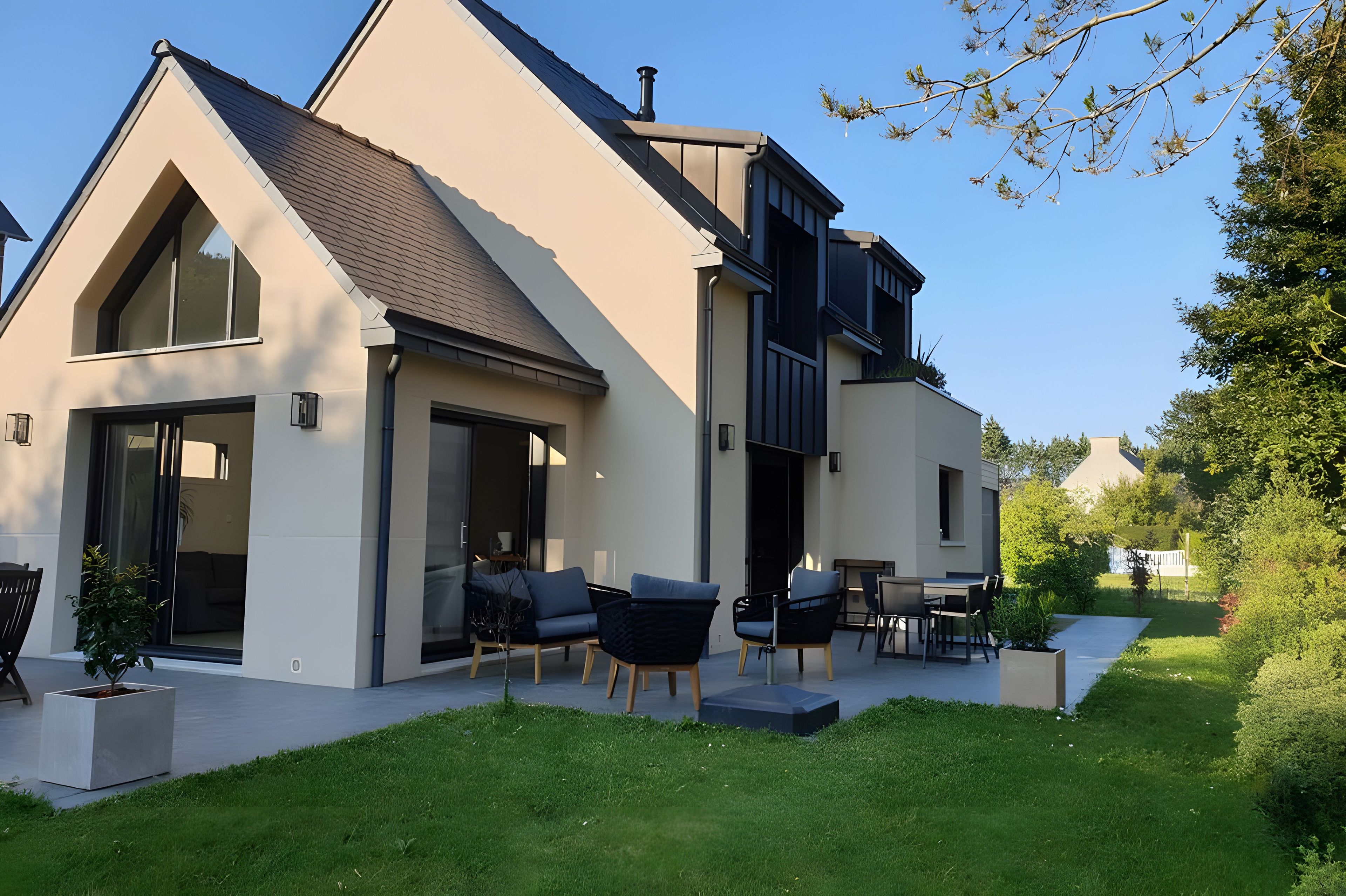 A modern two-story house with a large patio area, outdoor seating, and a well-maintained lawn.