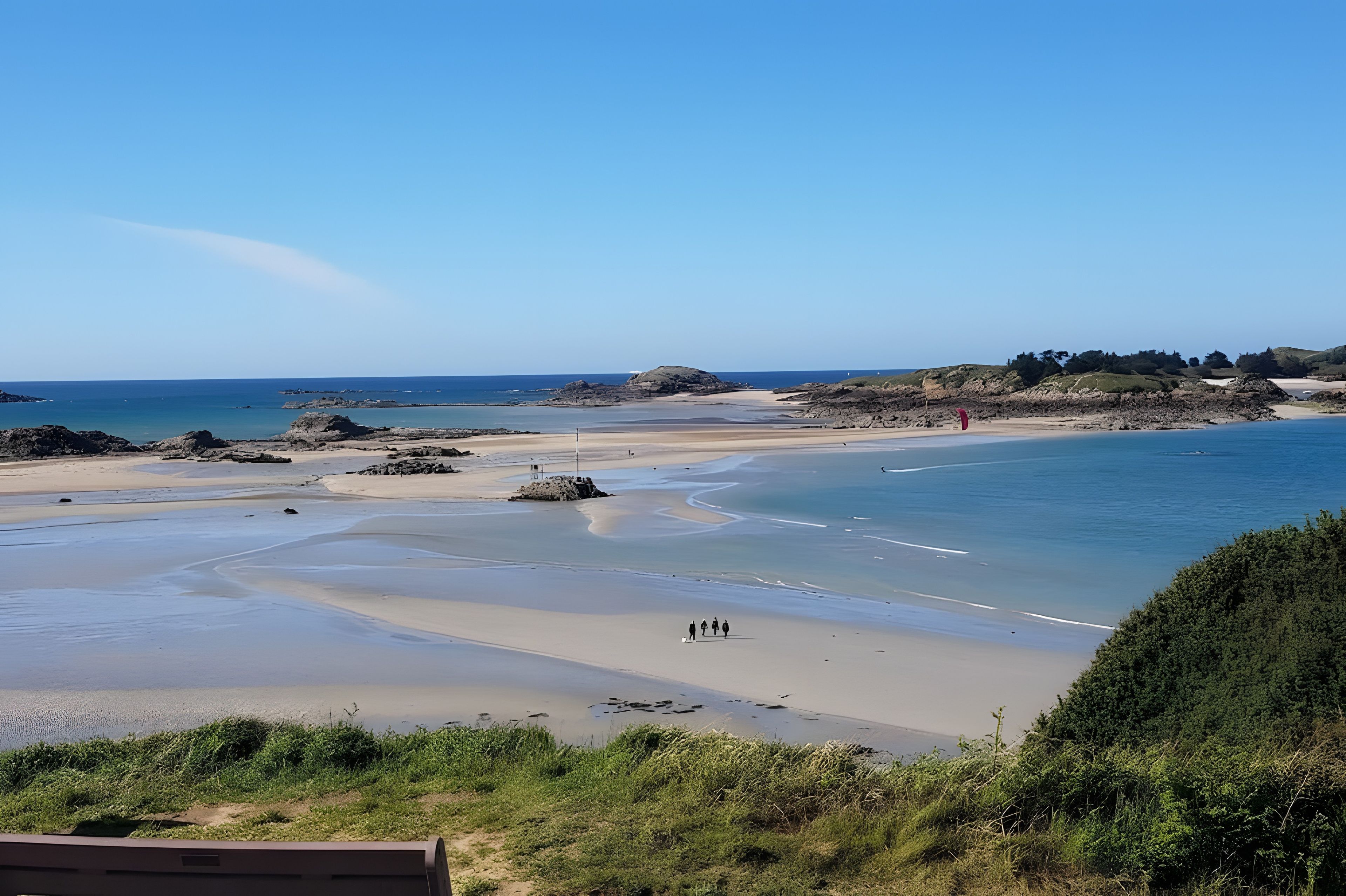 Eine Küstenlandschaft mit Sandstrand, ruhigem Wasser und blauem Himmel.