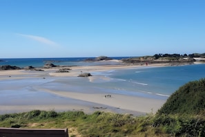 A coastal landscape with a sandy beach, calm waters, and a clear sky.