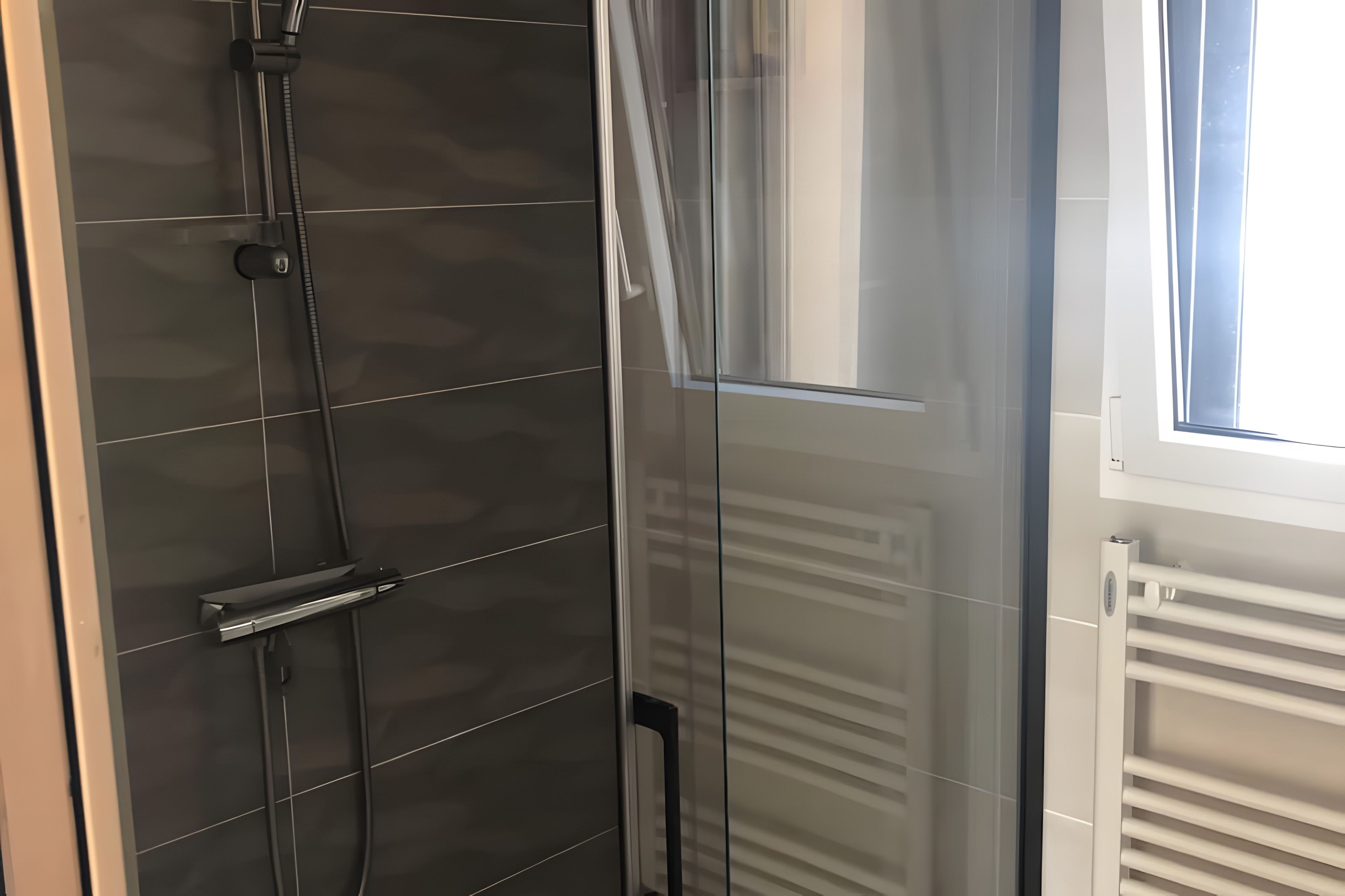 Ein modernes Badezimmer mit einer Duschkabine aus Glas, einem sichtbaren Handtuchhalter und einem Fenster, das für natürliches Licht sorgt.