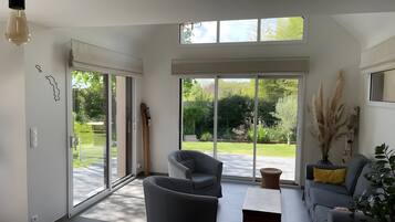 Una sala de estar moderna con un sofá gris, una mesa de centro y un amplio ventanal corredero que da a un jardín.