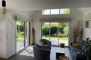 Una sala de estar moderna con un sofá gris, una mesa de centro y un amplio ventanal corredero que da a un jardín.