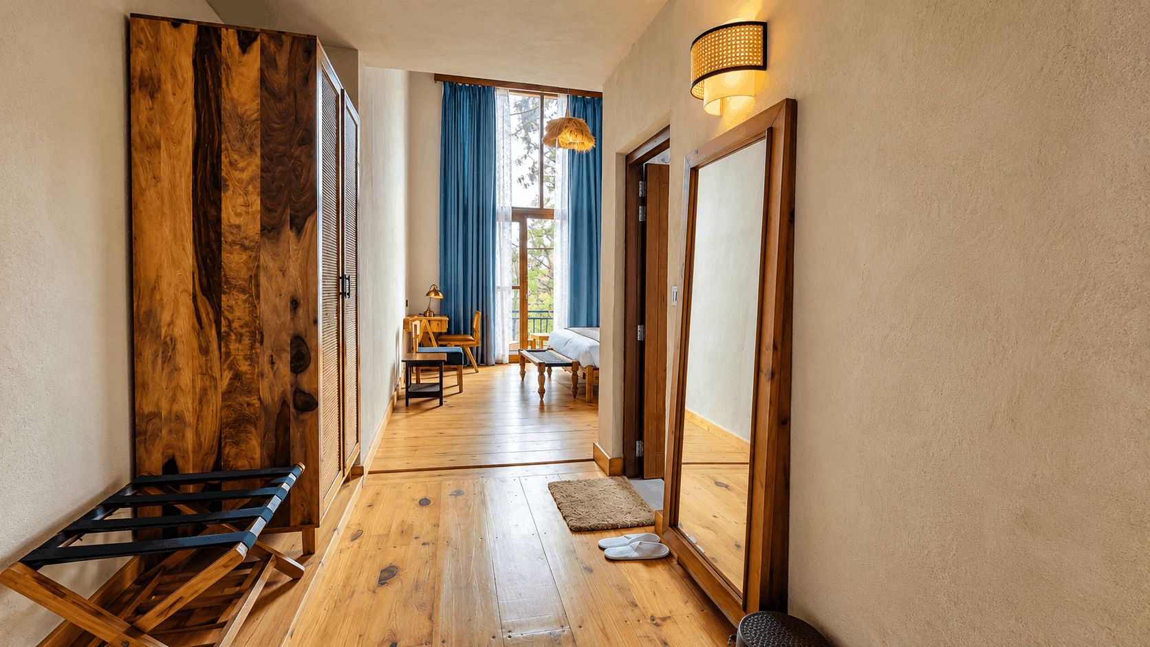 A hallway with wooden flooring, a mirror, a door, and a window with blue curtains.