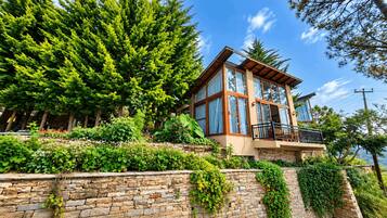 A modern house with a stone retaining wall, large windows, and a balcony.
