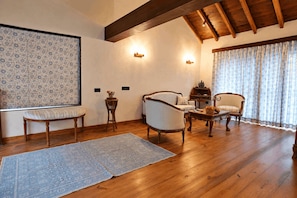 Una habitación con suelo de madera, dos sillones, un banco, una mesita y una alfombra estampada.