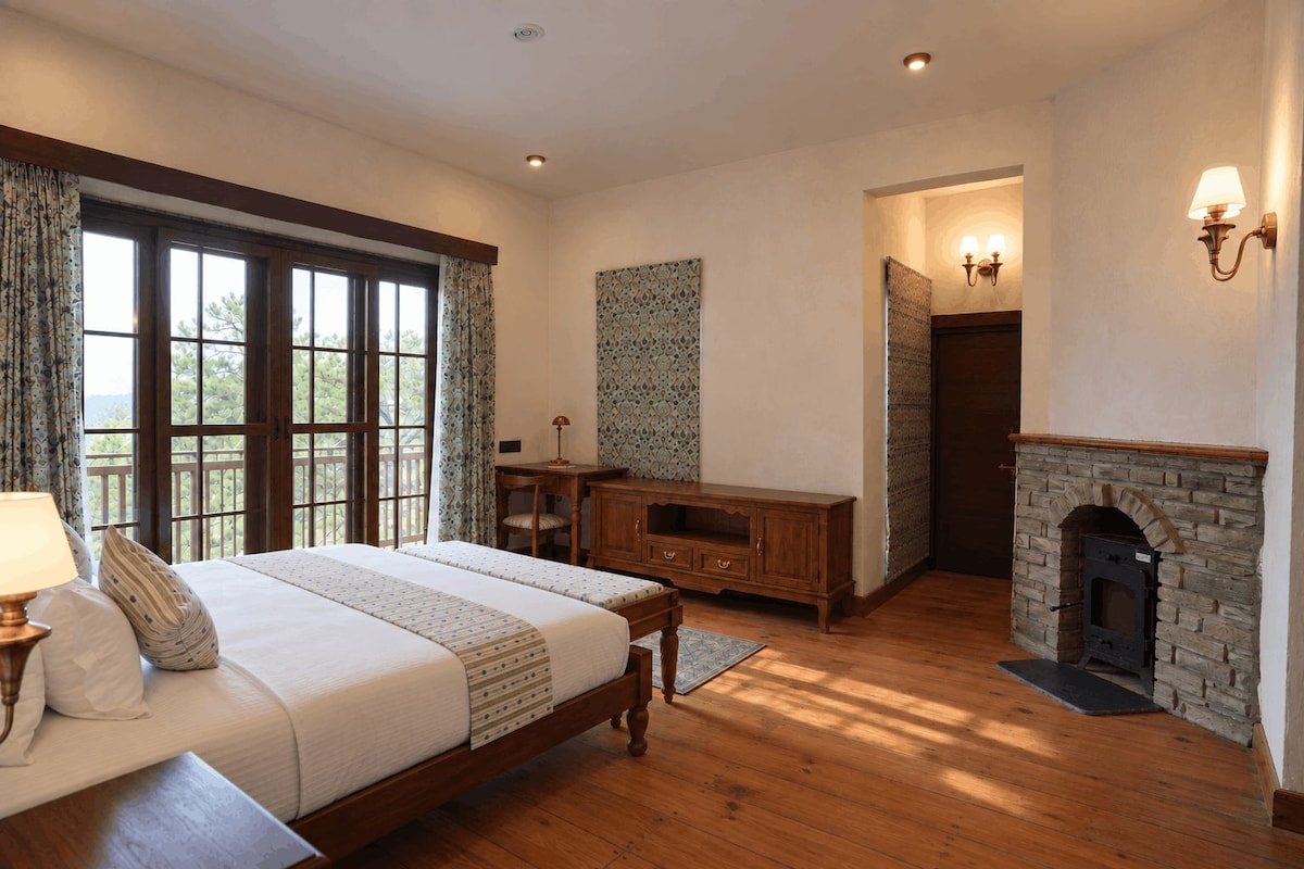 A bedroom with a large bed, wooden furniture, a fireplace, and a view through a window.