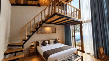 Un dormitorio con una escalera de madera, una cama con almohadas, una mesita de noche y vistas a través de un gran ventanal.