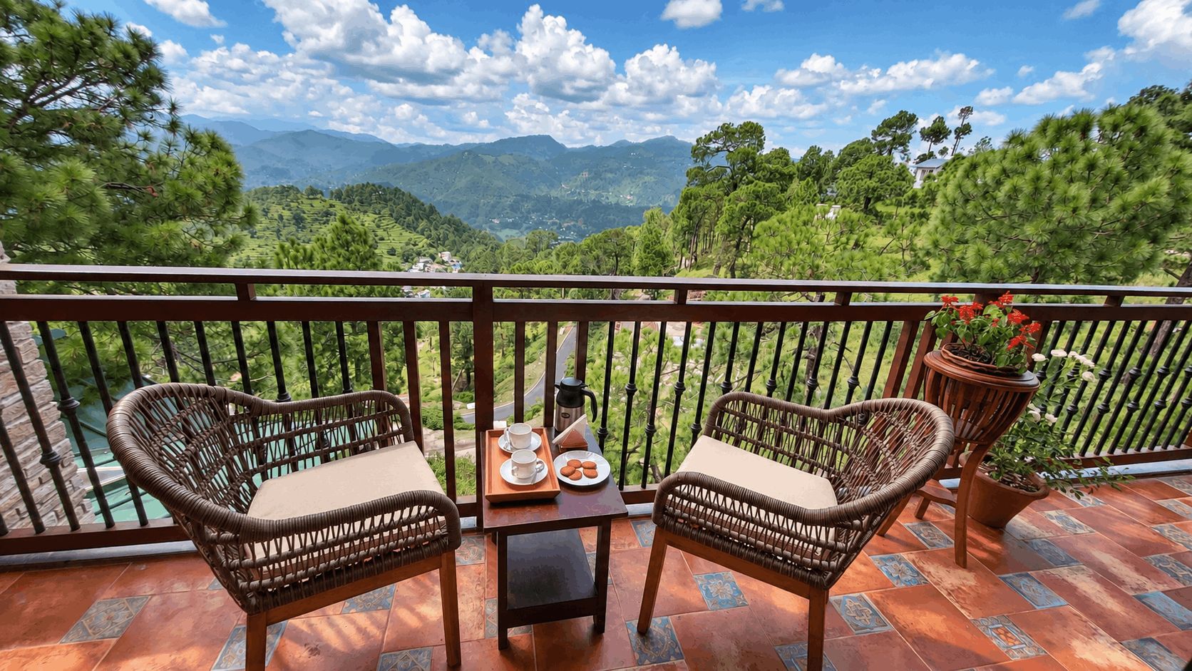 Un balcón con sillas de mimbre, una mesa y una bandeja con tazas y galletas.