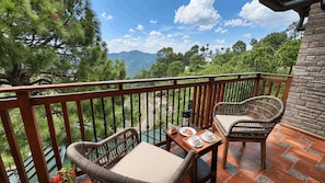 A balcony with wicker chairs, a wooden table, and a tray with cookies and cups. - The Camellia House Hotel (Almora)
