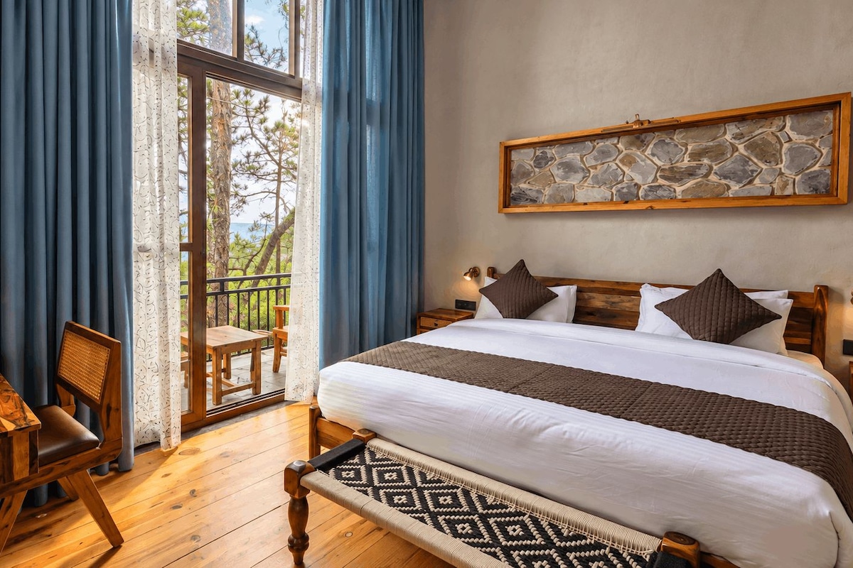 A bedroom with a bed, a wooden desk, a chair, a nightstand, and a stone wall art piece.