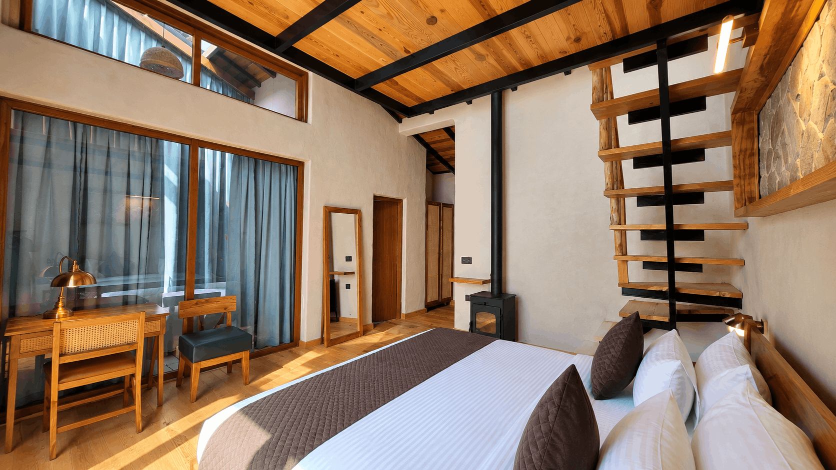 A bedroom with a large bed, wooden furniture, a desk, and a stone wall.